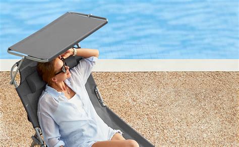 Oseba na vrtnem ležalniku ob bazenu z knjigo